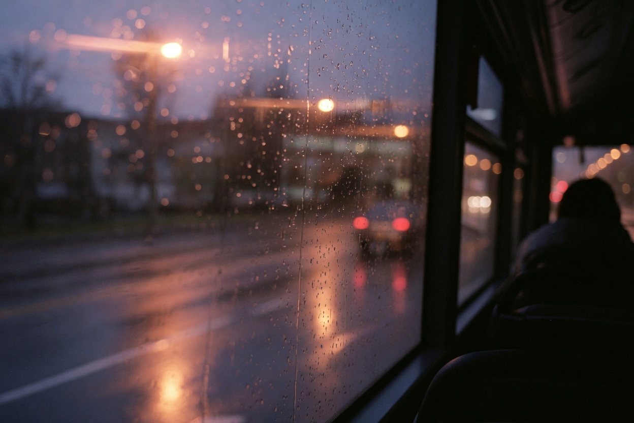 Rain on a bus window at night, with streetlights blurred beyond the glass